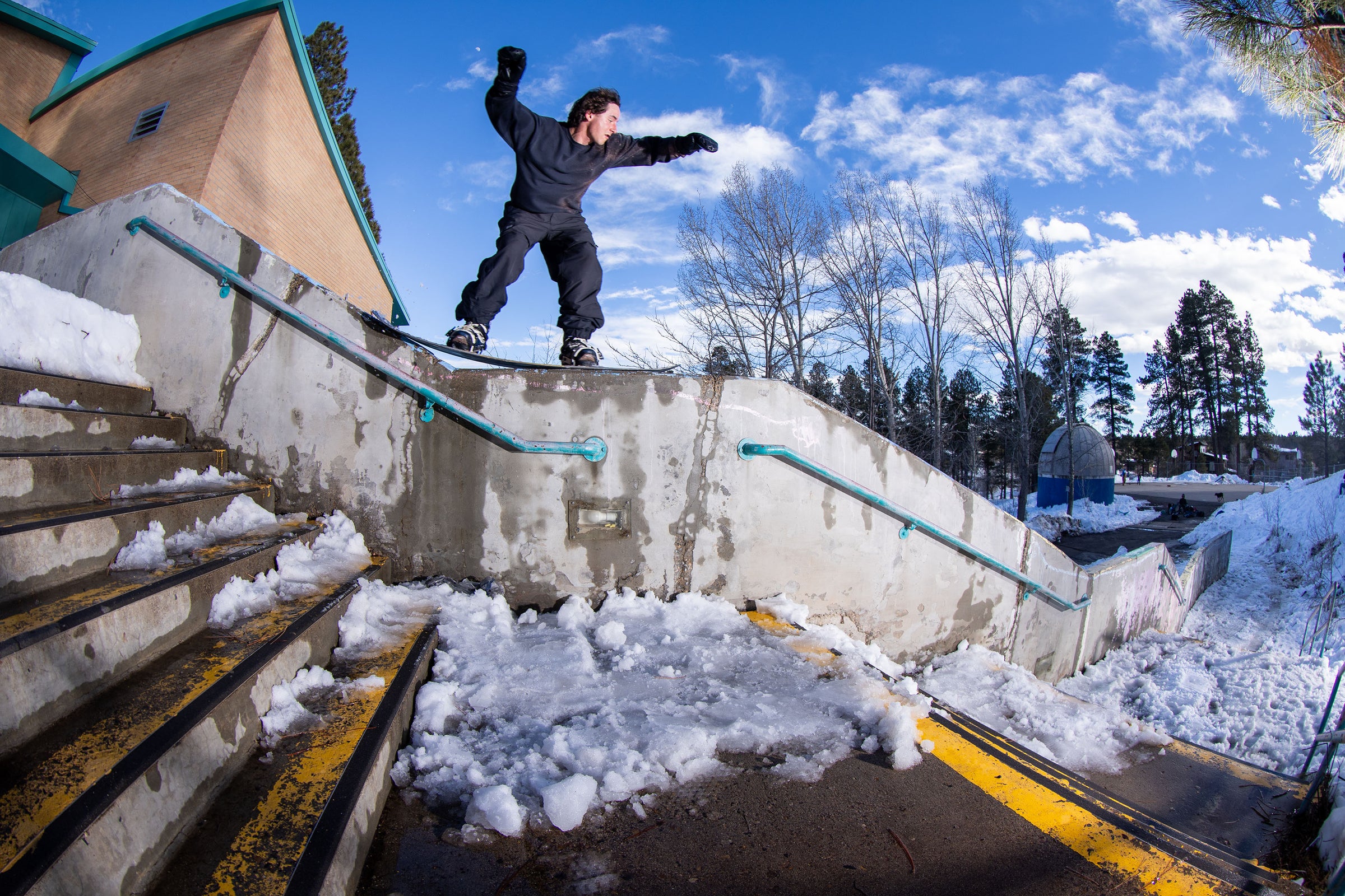 Caleb Kinnear 50-50 on a snow-covered staircase with a blue sky and trees in the background