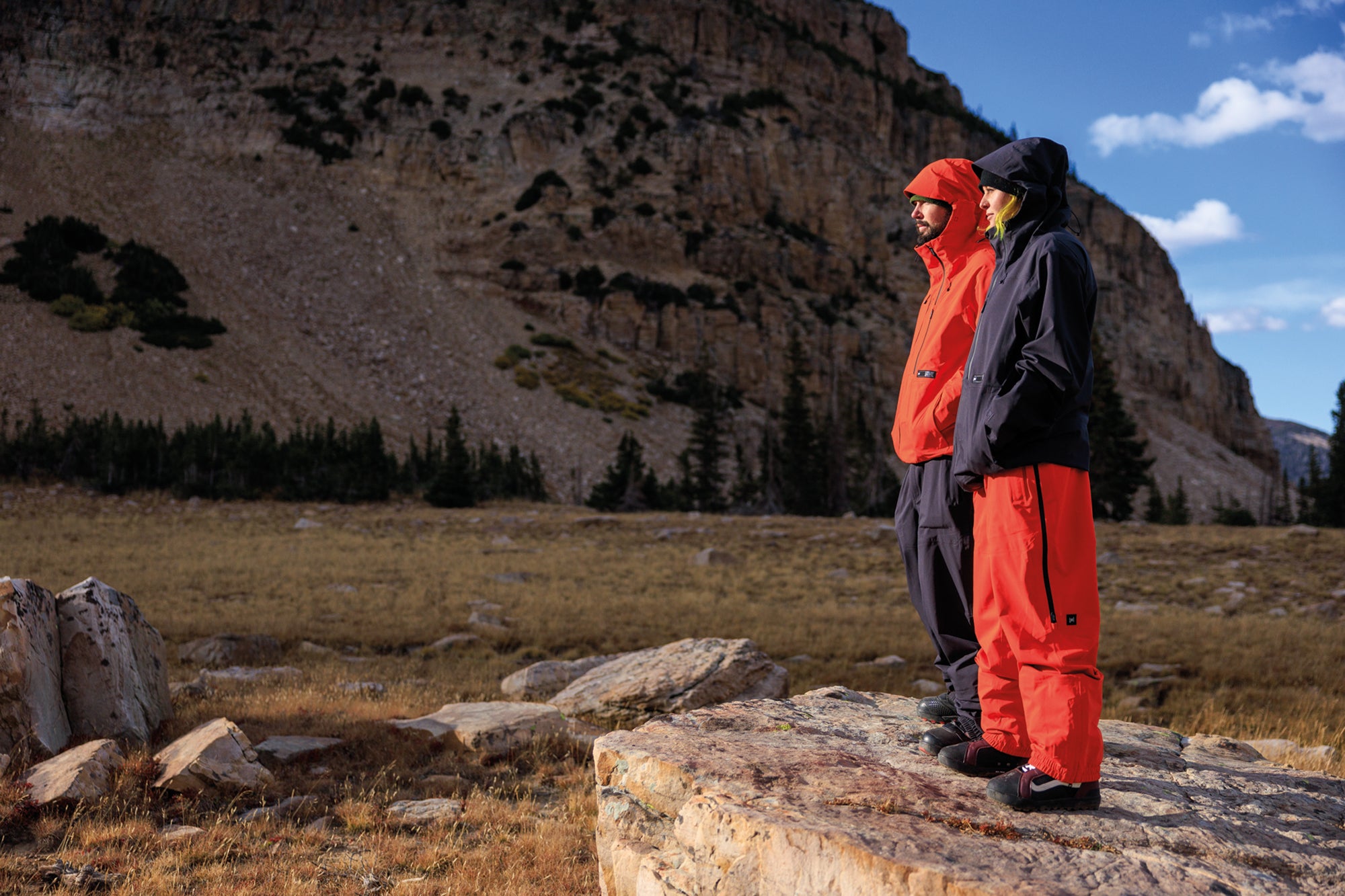 Axial Pro Kit: Two people in red and black snow gear standing on a rocky outcrop with mountains in the background.